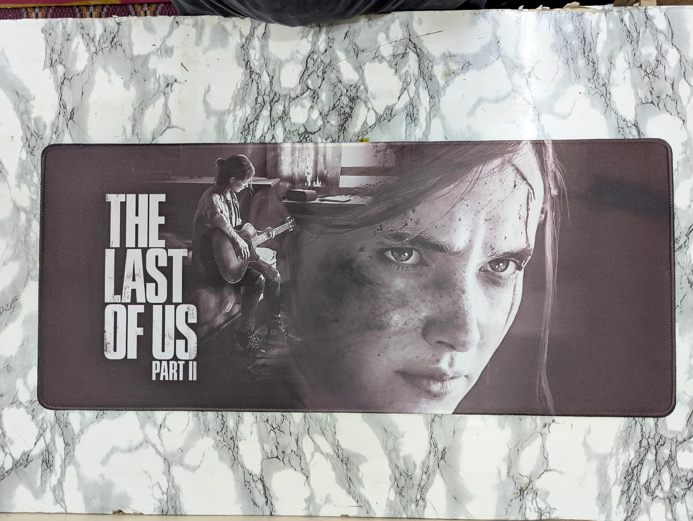 Extra-large desk mat in black and white featuring The Last of Us Part II artwork with Ellie playing guitar overlaid on a close-up portrait