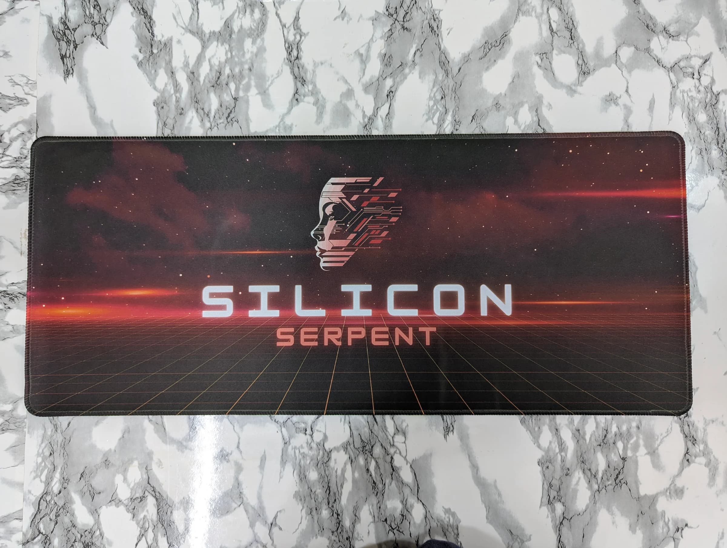 Desk mat with a retro-futuristic sci-fi design featuring a cybernetic profile face and 'Silicon Serpent' text over a glowing grid horizon